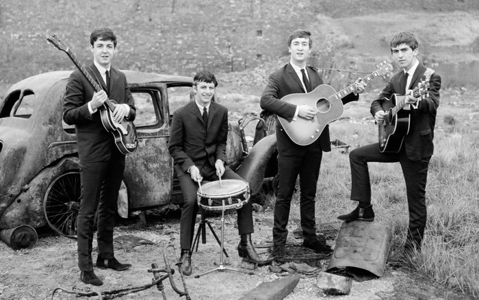 The Beatles posing with instruments near a wrecked car