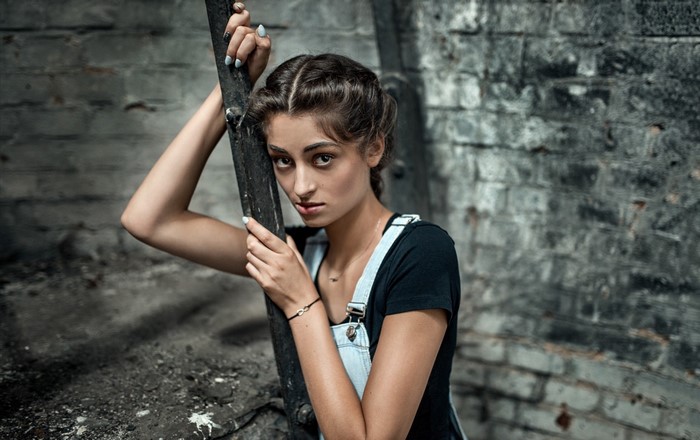 Woman in overalls leaning on a pole