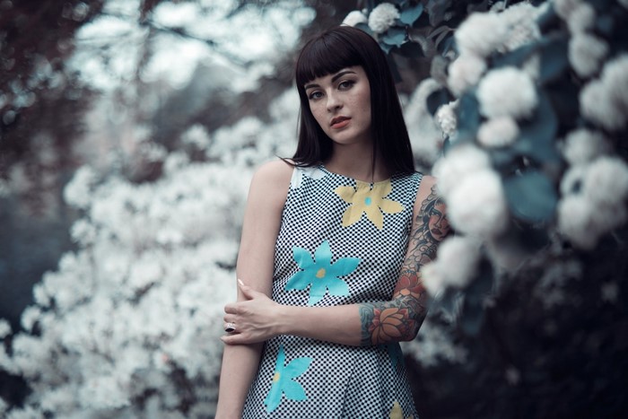 Woman with tattoos and floral dress in front of white flowers