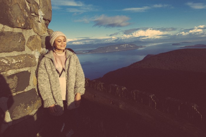 Woman in beanie and sweater on mountain overlooking water