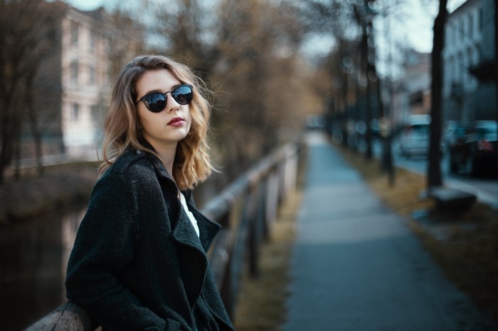 Woman wearing sunglasses and a coat standing by a railing