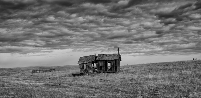 Abandoned house on a grassy plain under cloudy sky