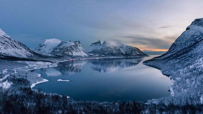 Snow-covered mountains reflecting in a calm fjord at dusk