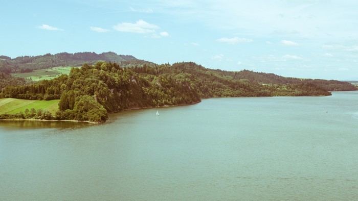 Sailboat on a large lake surrounded by forested hills