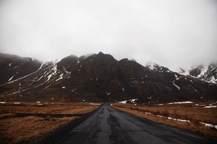 Road leading to snow-capped mountains under cloudy sky