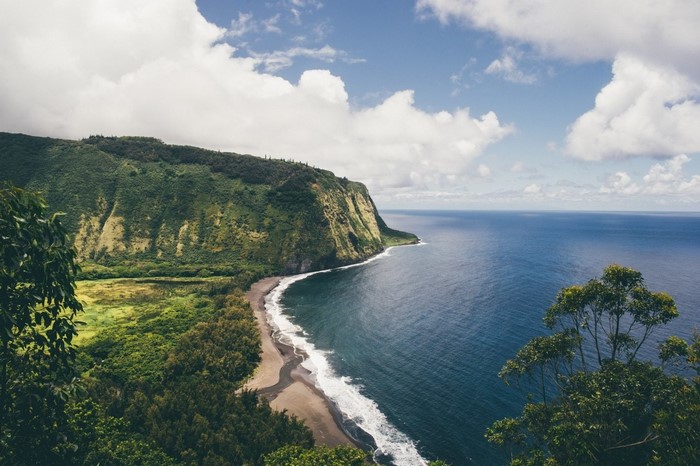 Green cliff overlooking a dark blue ocean with white waves
