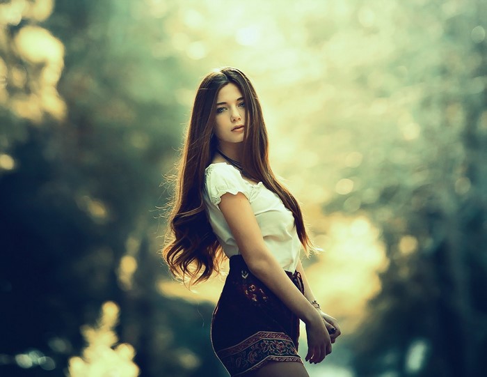 Young woman with long brown hair in a white top and patterned skirt