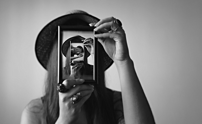 Woman in hat holding a mirror reflecting herself