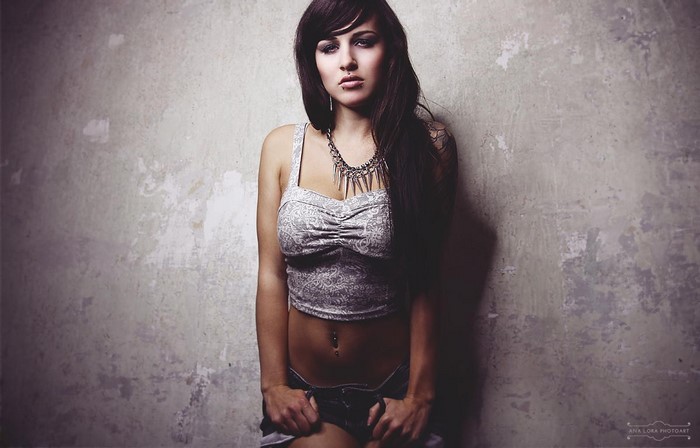Woman in crop top and shorts posing against a wall