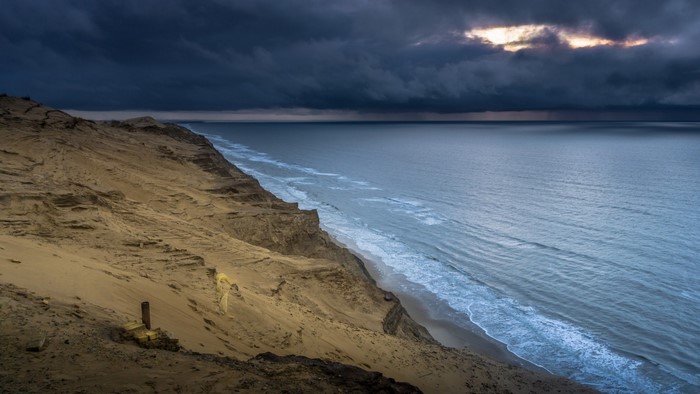 Sandy cliff overlooking the ocean under stormy clouds