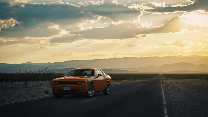 Orange Dodge Challenger on a desert road at sunset
