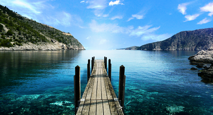 Wooden pier extending into a clear blue sea with mountains
