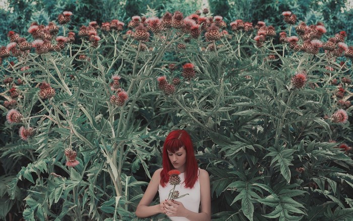 Woman with red hair holding a flower in a garden