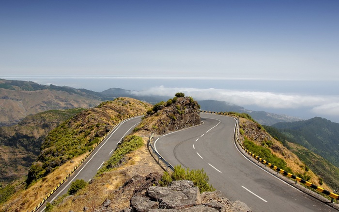 Winding mountain road overlooking ocean and clouds