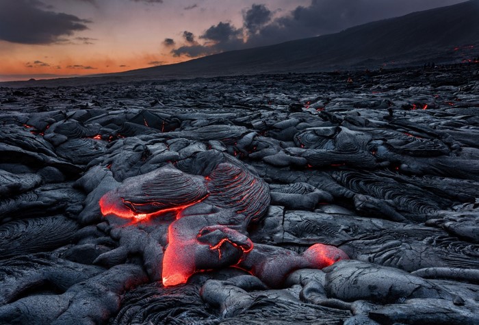Molten lava flowing over dark volcanic rock landscape at sunset