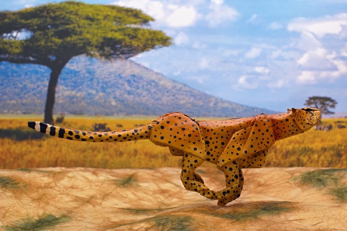 Origami cheetah running in savanna landscape