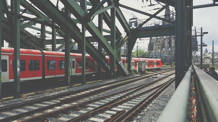 Red trains under a green bridge with Cologne Cathedral in the background