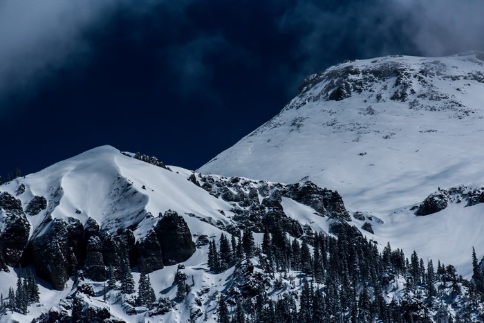 Snowy mountain range with dark clouds and pine trees