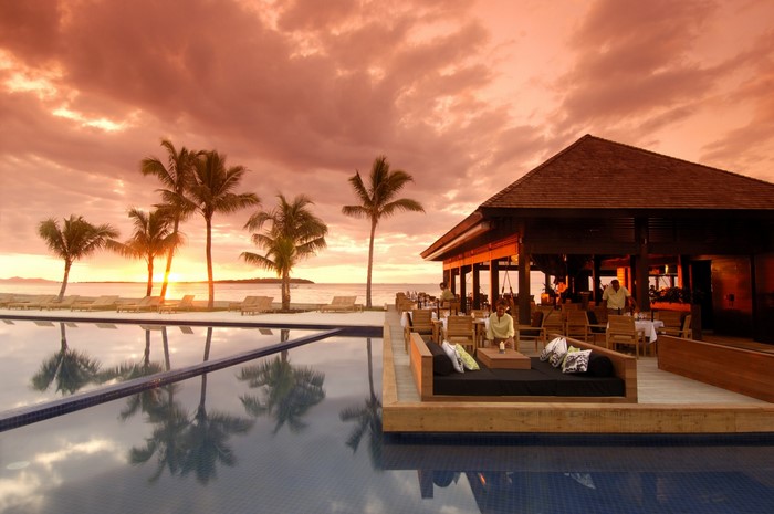 Resort with swimming pool and palm trees at sunset