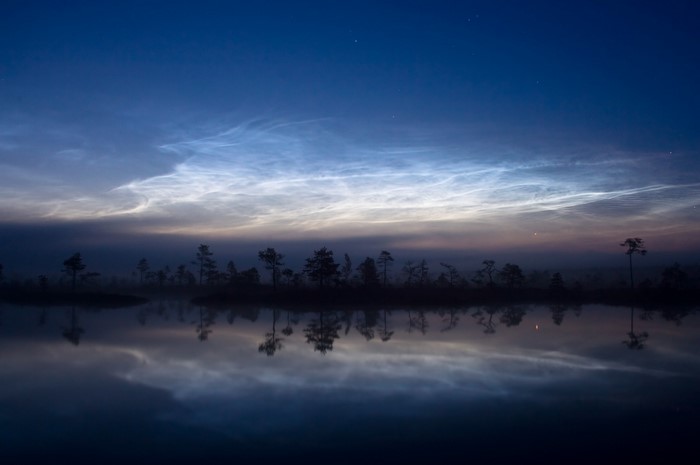 Noctilucent clouds over a misty wetland lake at dawn