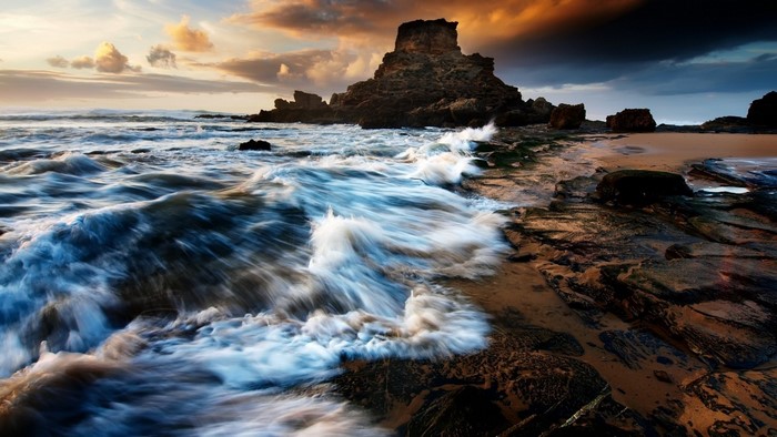 Waves crashing on rocky shore at sunset