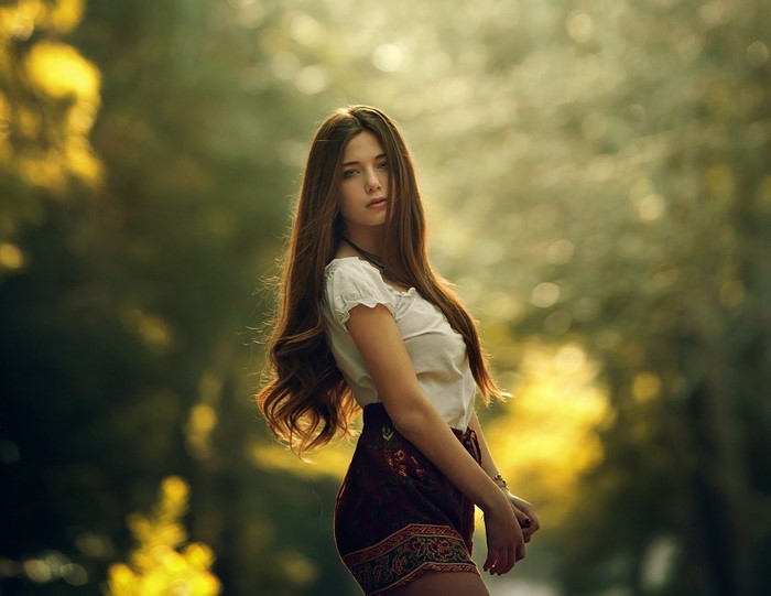 Woman with long brown hair in a white top and patterned skirt outdoors