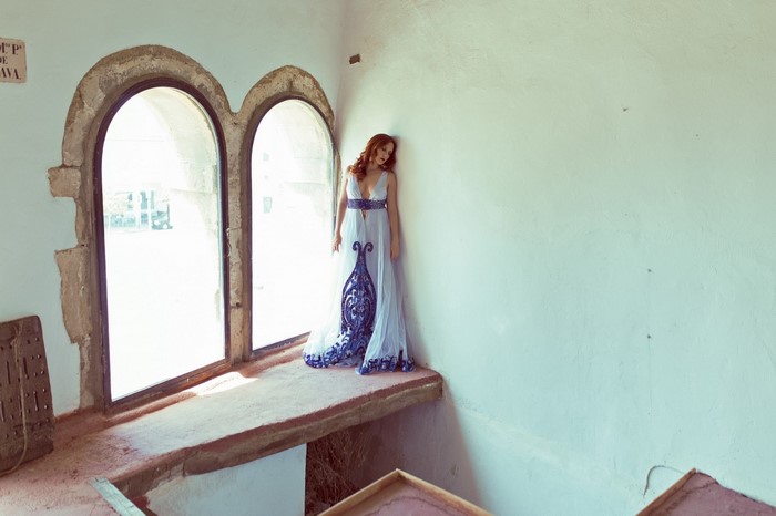 Woman in blue and white dress by arched window