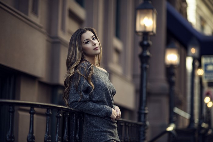 Woman in Cozy Sweater Sitting by Street Lamp at Dusk