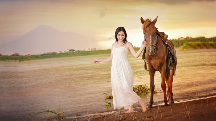 Woman in white dress with horse by the water