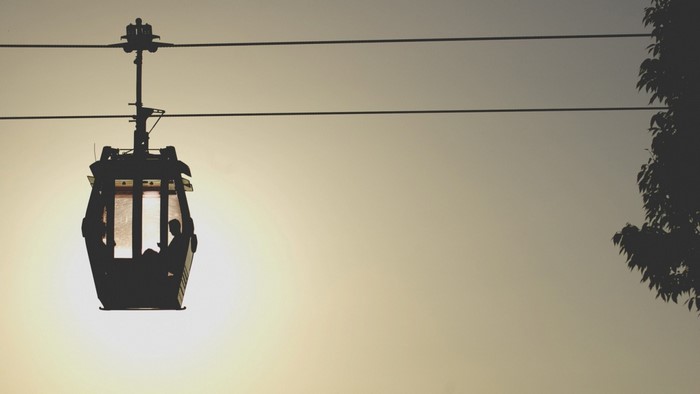 Silhouette of a cable car with a person inside against a bright sky