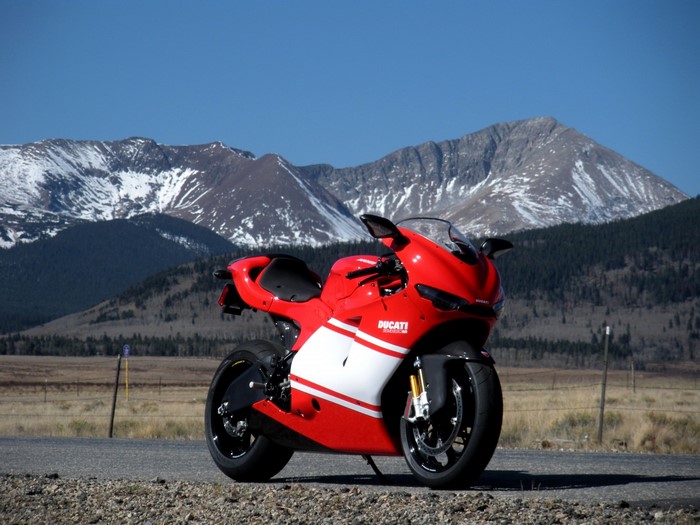 Red Ducati motorcycle parked on a road with mountains