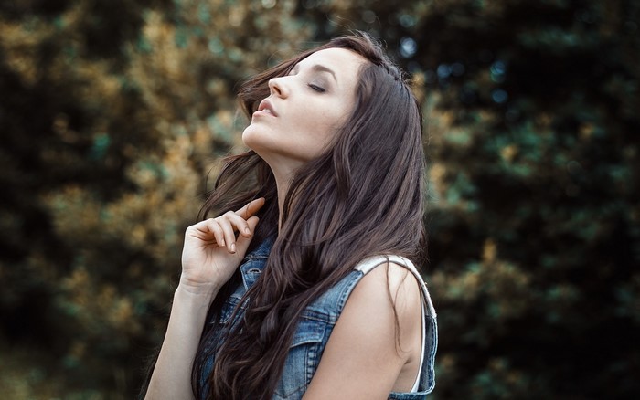 Woman with long brown hair in denim vest