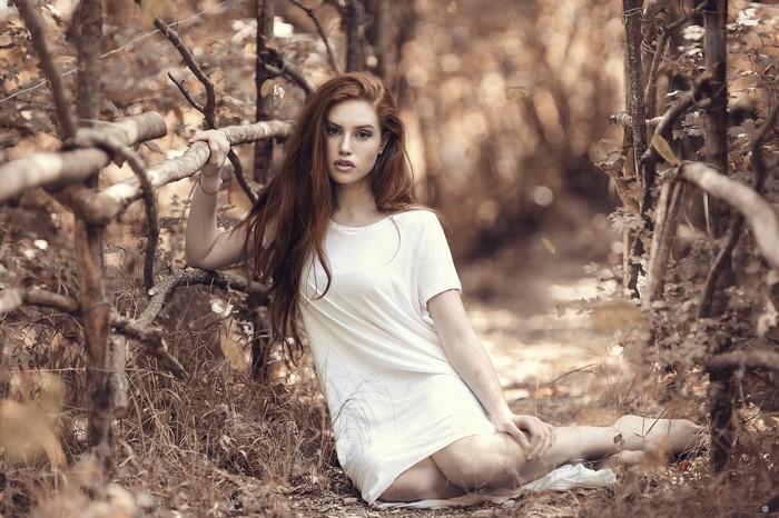 Woman with long red hair in a white dress in a forest