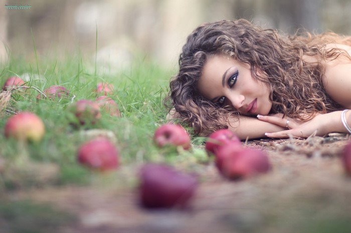 Woman with curly hair lying in grass with apples