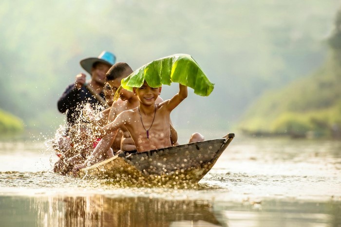 Boys in a boat with a banana leaf on a river