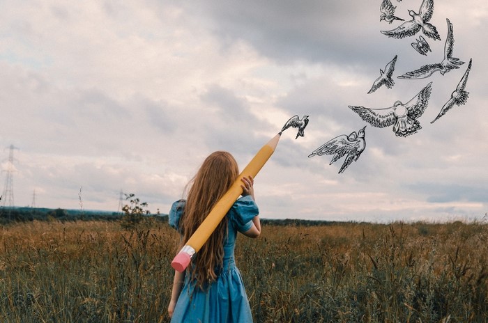 Girl drawing birds with a giant pencil in a field
