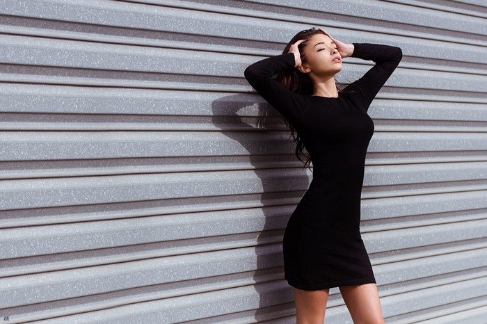 Woman in black dress leaning against a wall