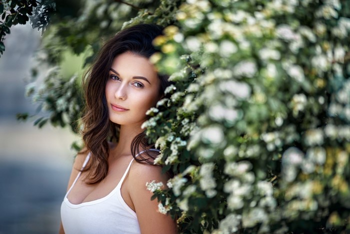 Woman with long brown hair in a white tank top near flowers