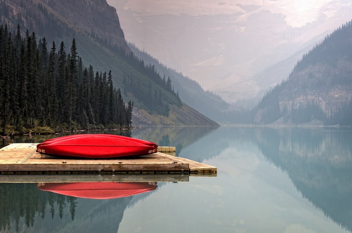 Red canoe on a dock at a misty mountain lake