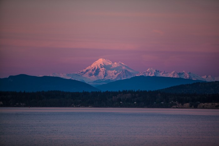 Snow-capped mountains at sunset over a calm sea