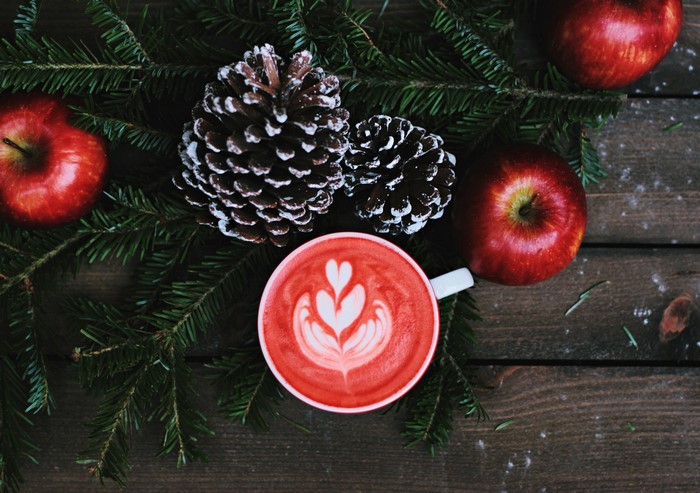Red latte with apples and pine cones on wood