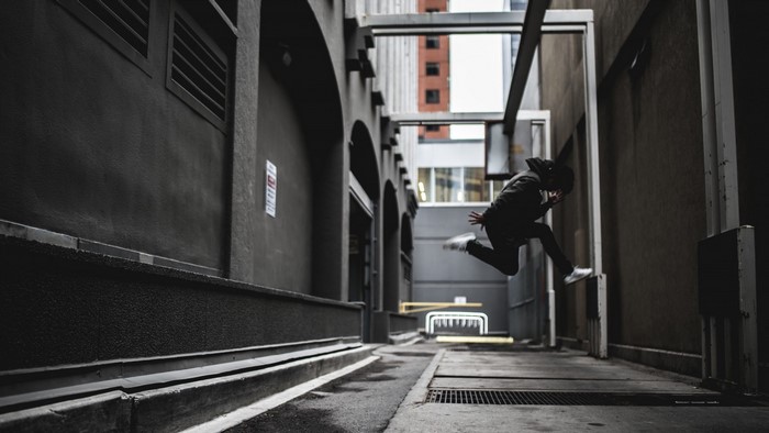 Man in black hoodie jumping in urban alley