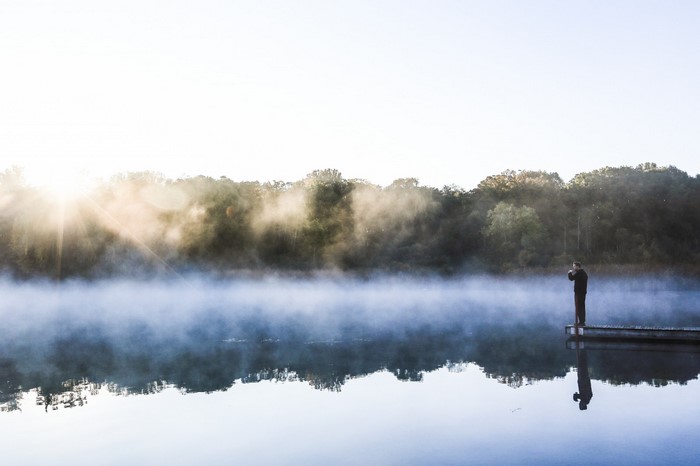Man on a dock at sunrise with mist over the lake