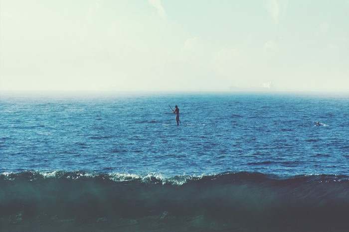 Person paddleboarding on the ocean with waves