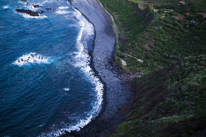 Aerial view of a rocky coastline with waves and green cliffs