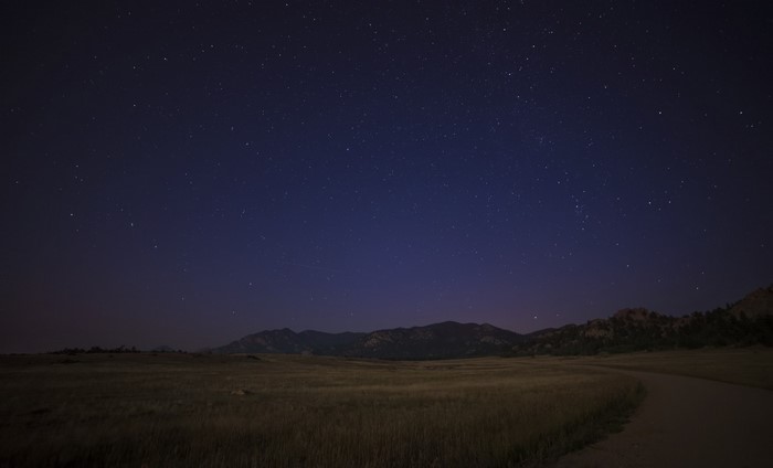 Night sky over a grassy field and mountains
