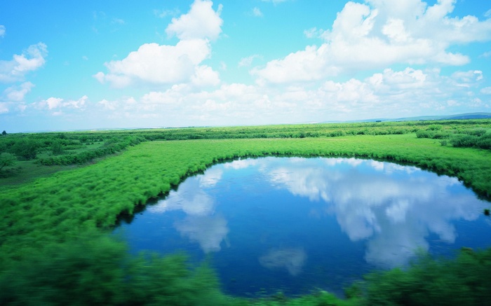 A tranquil lake reflects the sky and clouds amidst green fields.