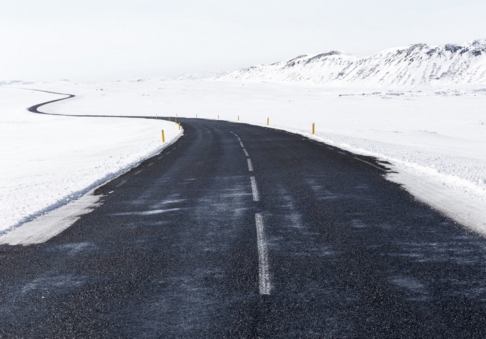 Winding asphalt road through a snowy landscape with mountains