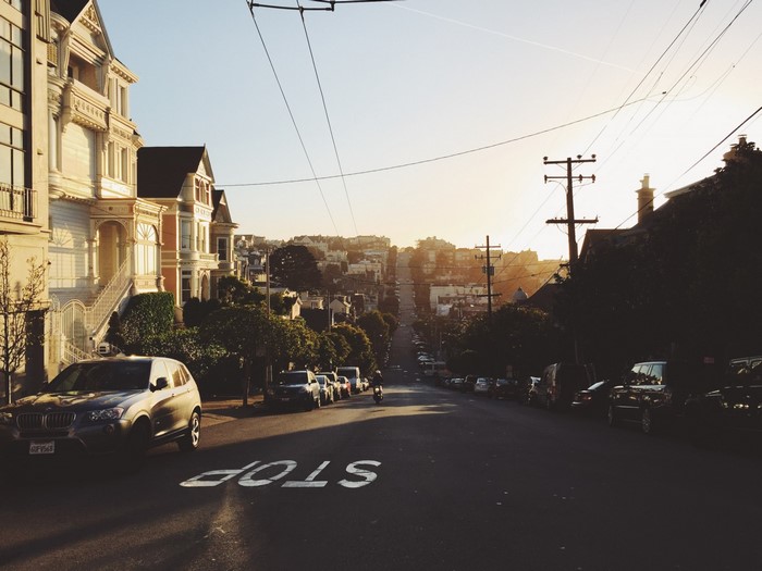 San Francisco street with Victorian houses and cars at sunset