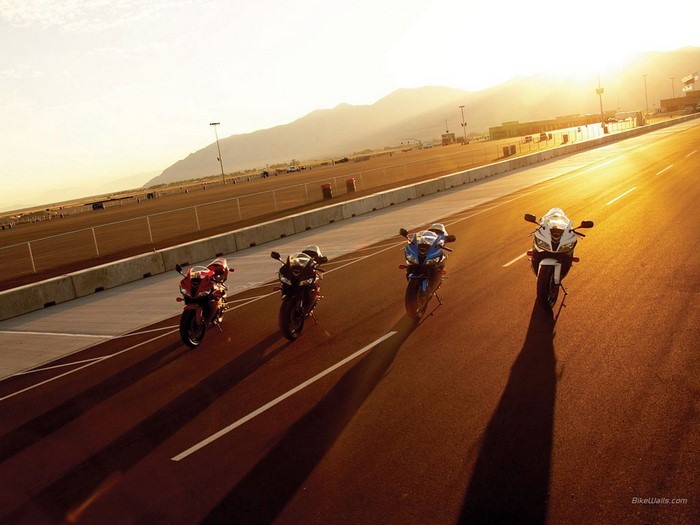 Four Honda motorcycles lined up on a racetrack at sunset